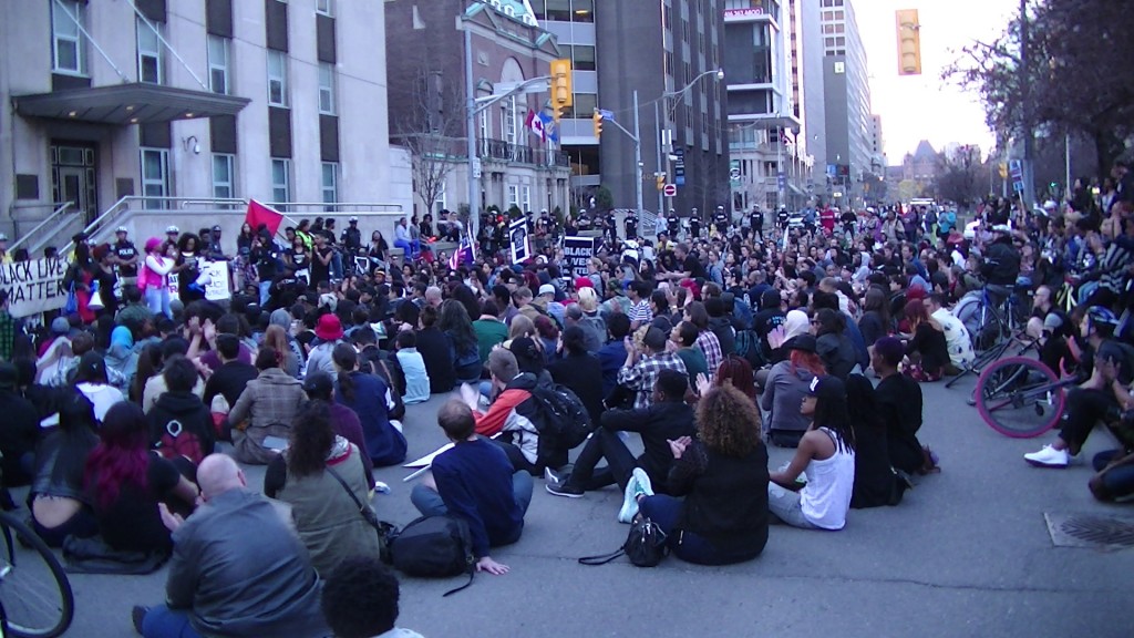 Protesters sit-down blocking University Ave in front of the US Consulate